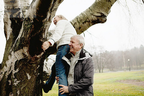 Senior Mann hilft Frau im Park auf den Baum klettern