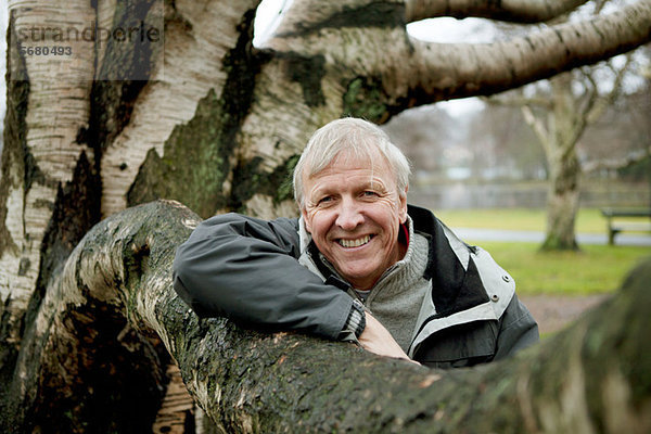 Älterer Mann an Baum gelehnt  lächelnd