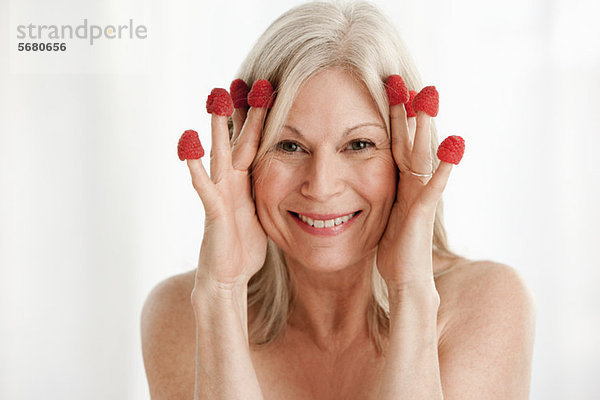 Reife Frau mit Himbeeren an den Fingern