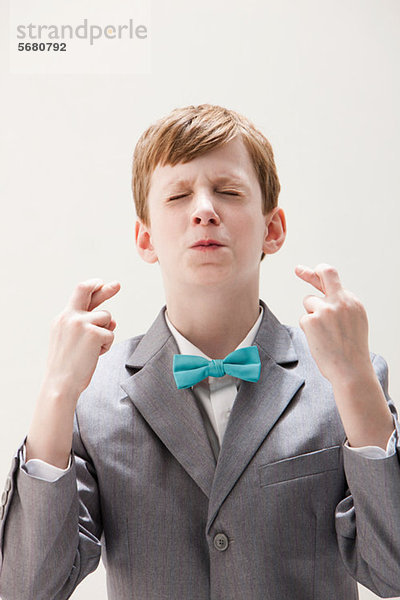 Junge im grauen Anzug mit gekreuzten Fingern  Studioaufnahme