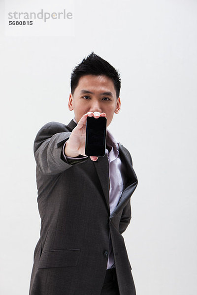 Junger asiatischer Geschäftsmann hält Handy  Studioaufnahme