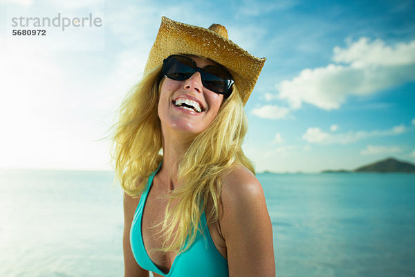 Glückliche Frau mit Sonnenbrille und Cowboyhut am Meer