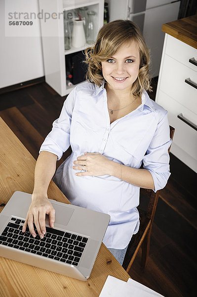 Schwangere Frau mit Laptop in der Küche