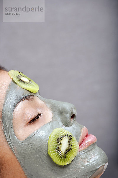 Frau mit Hautmaske und Kiwi im Bad