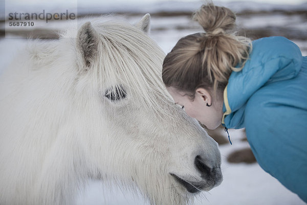 Frau küsst weißes Pferd im Schnee