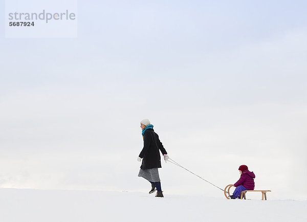 Mutter zieht Tochter auf Schlitten im Schnee