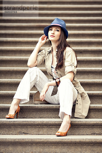 Frau mit Hut sitzt auf einer Treppe