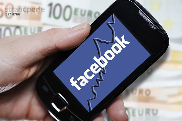 Hand mit Smartphone und Facebook-Logo vor Euroscheinen  Symbolbild Börsengang von Facebook