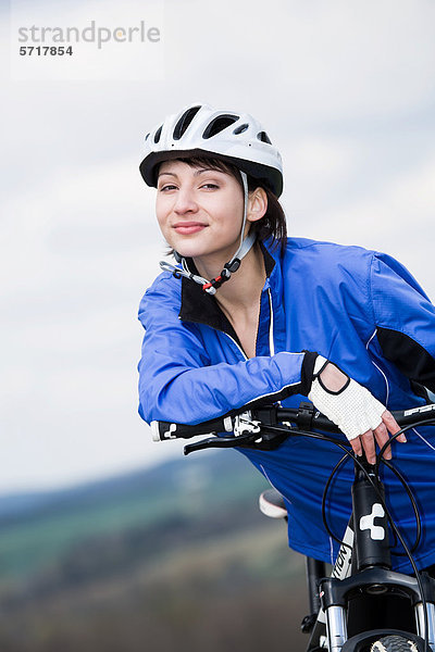 Frau mit Fahrradhelm stützt sich auf ihr Fahrrad