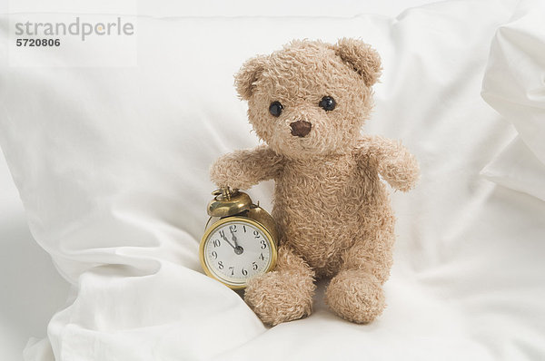 Teddybär mit Wecker auf dem Bett