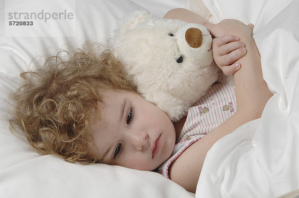 Krankes Mädchen im Bett liegend mit Teddybär