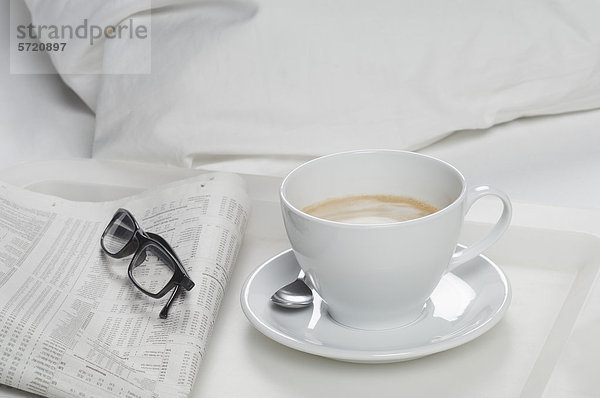 Tablett mit Kaffee mit Zeitung und Brille auf dem Bett  Nahaufnahme
