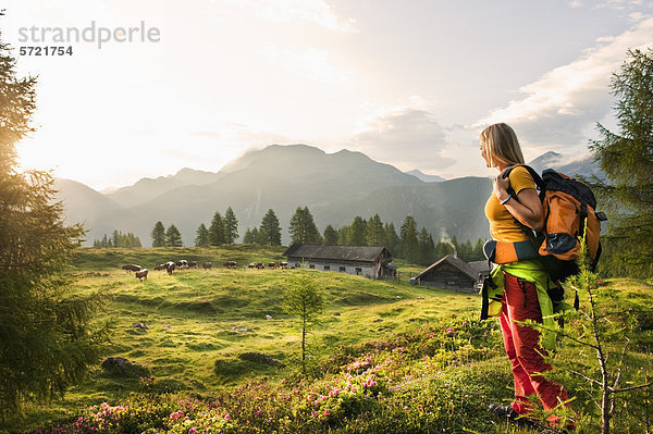 Österreich  Salzburger Land  Junge Frau auf der Alm stehend und Landschaft beobachtend