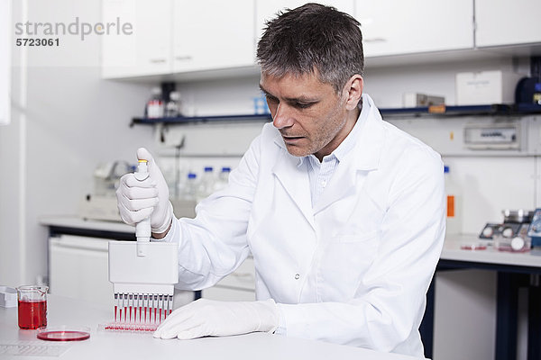 Deutschland  Bayern  München  Wissenschaftler gießt rote Flüssigkeit mit Pipette in Testschale für die medizinische Forschung im Labor