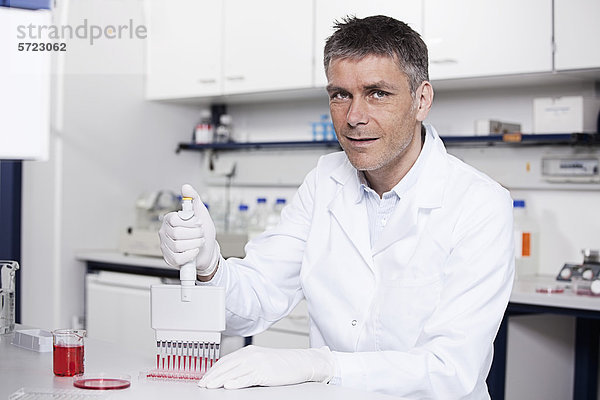 Deutschland  Bayern  München  Wissenschaftler gießt rote Flüssigkeit mit Pipette in Testschale für die medizinische Forschung im Labor