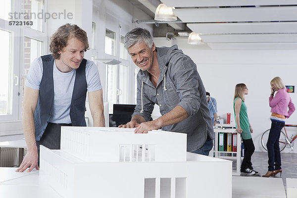 Männer beobachten Architekturmodell im Büro  Kollegen sprechen im Hintergrund