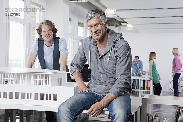 Männer mit Architekturmodell im Büro  Kollegen sprechen im Hintergrund