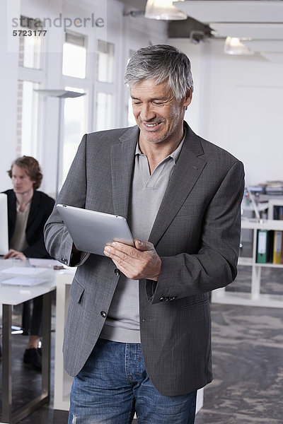 Erwachsener Mann mit digitalem Tablett  Kollege arbeitet im Hintergrund