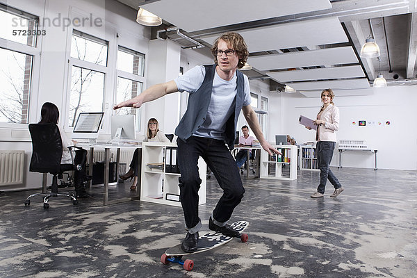 Man Skate Boarding im Büro  während die Kollegen im Hintergrund arbeiten.