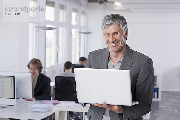Erwachsener Mann mit Laptop  Kollegen  die im Hintergrund arbeiten