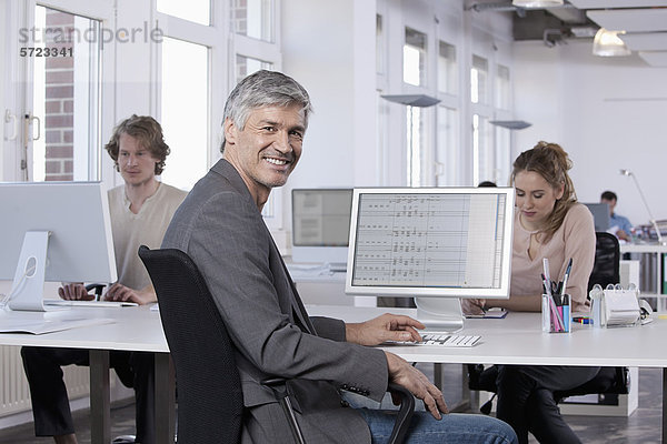 Reifer Mann lächelt  Kollegen arbeiten im Hintergrund