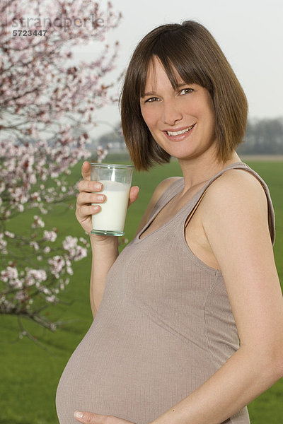 Deutschland  Nordrhein-Westfalen  Schwangere mit Milchglas  lächelnd  Portrait