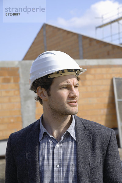 Junger Mann mit Schutzhelm auf der Baustelle stehend