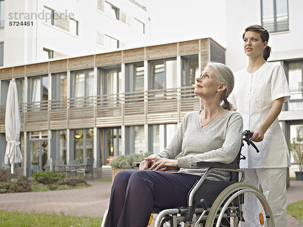 Hausmeisterin schiebt ältere Frauen im Rollstuhl