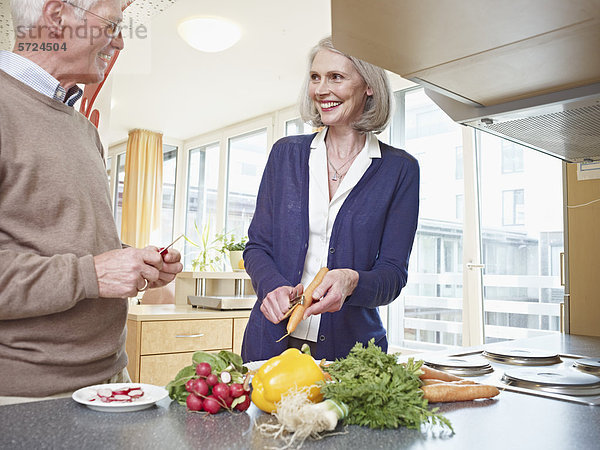 Deutschland  Köln  Seniorenpaar beim Gemüse schneiden  lächelnd