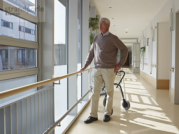 Senior im Flur des Pflegeheims stehend  Gehhilfe im Hintergrund