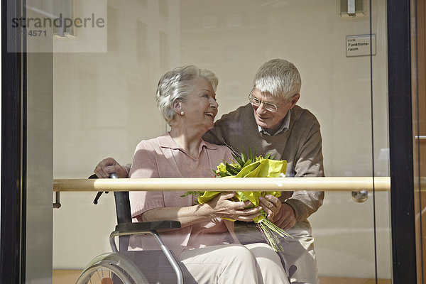 Seniorin im Rollstuhl mit Blumenstrauß  Mann lächelnd