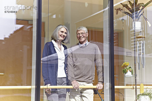 Deutschland  Köln  Seniorenpaar schaut durchs Fenster  lächelnd
