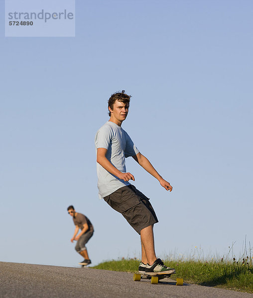 Österreich  Junge Männer beim Longboarding auf der Straße