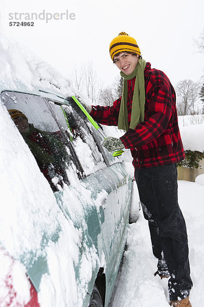 Österreich  Junger Mann beim Putzen von Schnee am Auto