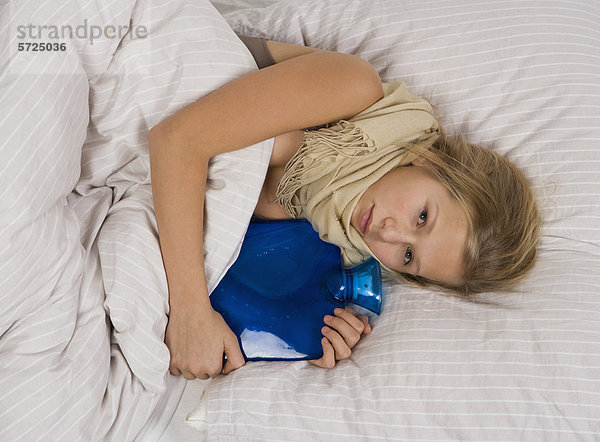 Teenagermädchen auf dem Bett liegend mit Wärmflasche