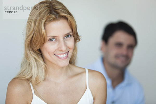 Lächelnde junge Frau im Hemd  Mann im Hintergrund