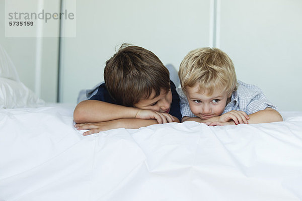 Junge Brüder liegen nebeneinander auf dem Bett  die Köpfe ruhen auf den Armen.