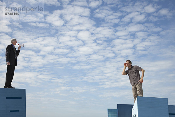 Überdimensionale Männer  die auf Dächern stehen  einer spricht durch ein Megaphon.