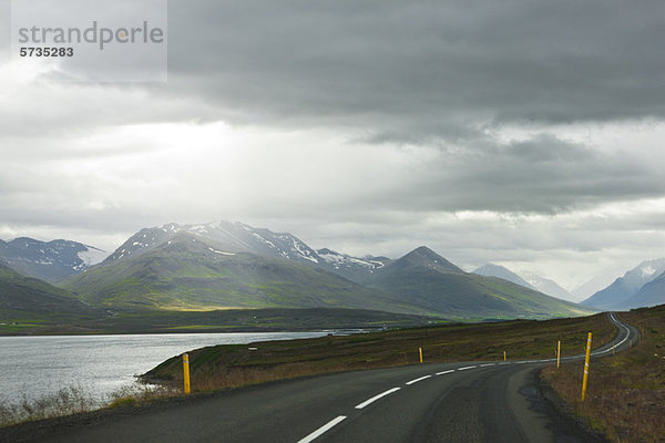 Island  Straße durch ruhige Landschaft mit Bergen im Hintergrund