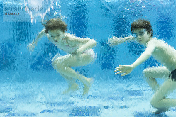 Geschwister schwimmen unter Wasser im Schwimmbad