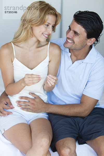 Mann  der die Hand auf den Bauch der Frau legt  nachdem er das Ergebnis des Schwangerschaftstests gelesen hat.