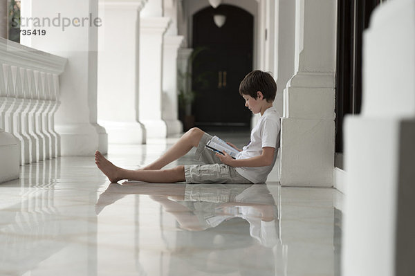 Junge sitzt auf dem Boden der Veranda und liest Buch.
