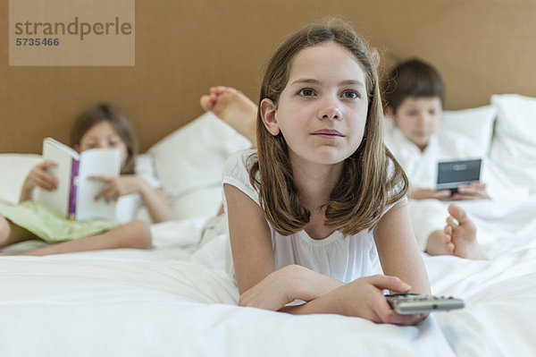 Mädchen auf dem Bett liegend und fernsehen  Geschwister im Hintergrund
