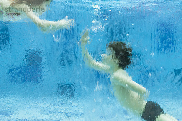 Geschwister spielen unter Wasser im Schwimmbad