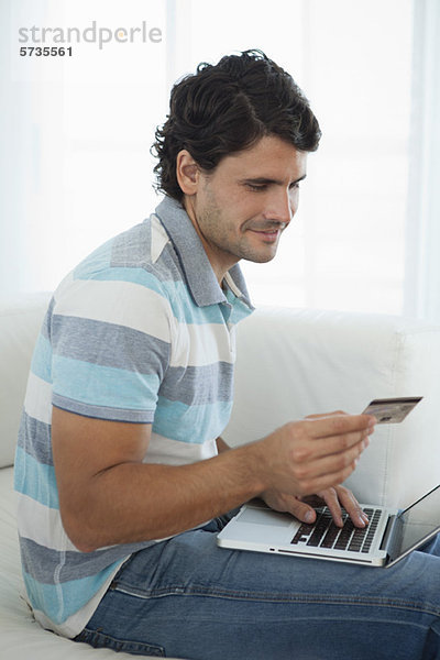 Mittlerer Erwachsener Mann  der eine Kreditkarte hält  während er einen Laptop benutzt.