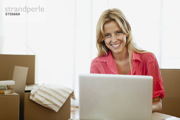 Junge Frau mit Laptop im neuen Haus mit Pappkartons