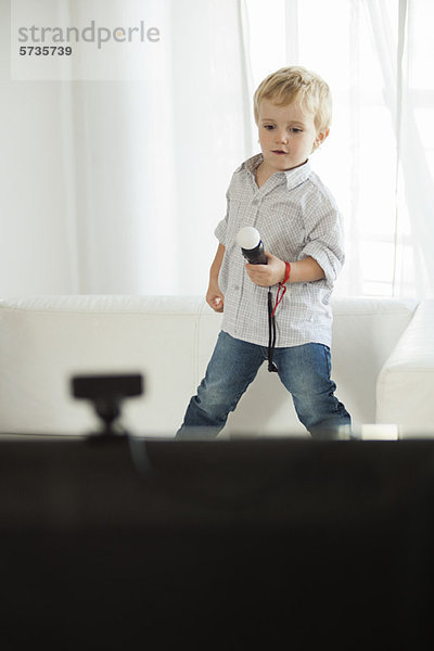 Kleiner Junge steht auf dem Sofa und hält ein Spielzeugmikrofon.