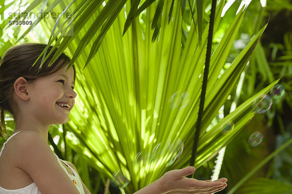 Mädchen spielt mit Blasen unter Palmblättern