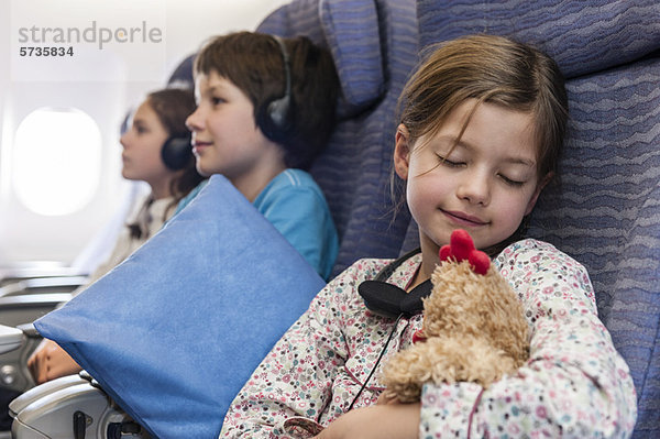 Mädchen schläft im Flugzeug mit Plüschtier