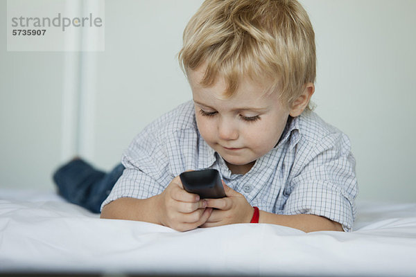 Kleiner Junge auf dem Bett liegend mit Handy